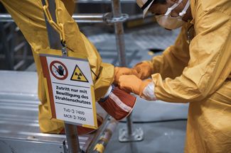 Ein Strahlenschutzmitarbeitender hilft einem Mitarbeitenden beim Ausziehen der Schutzkleidung