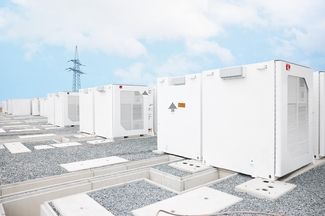 Auf dem Bild ist ein weisser Batteriepeicher vor einem Strommasten zu sehen.